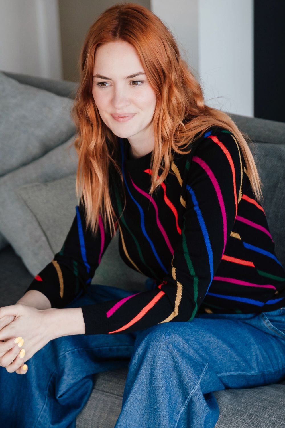 Woman wearing a colorful striped sweater sitting on a couch.