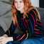 Woman wearing a colorful striped sweater sitting on a couch.