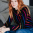 Woman wearing a colorful striped sweater sitting on a couch.
