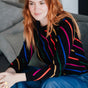 Woman wearing a colorful striped sweater sitting on a couch.