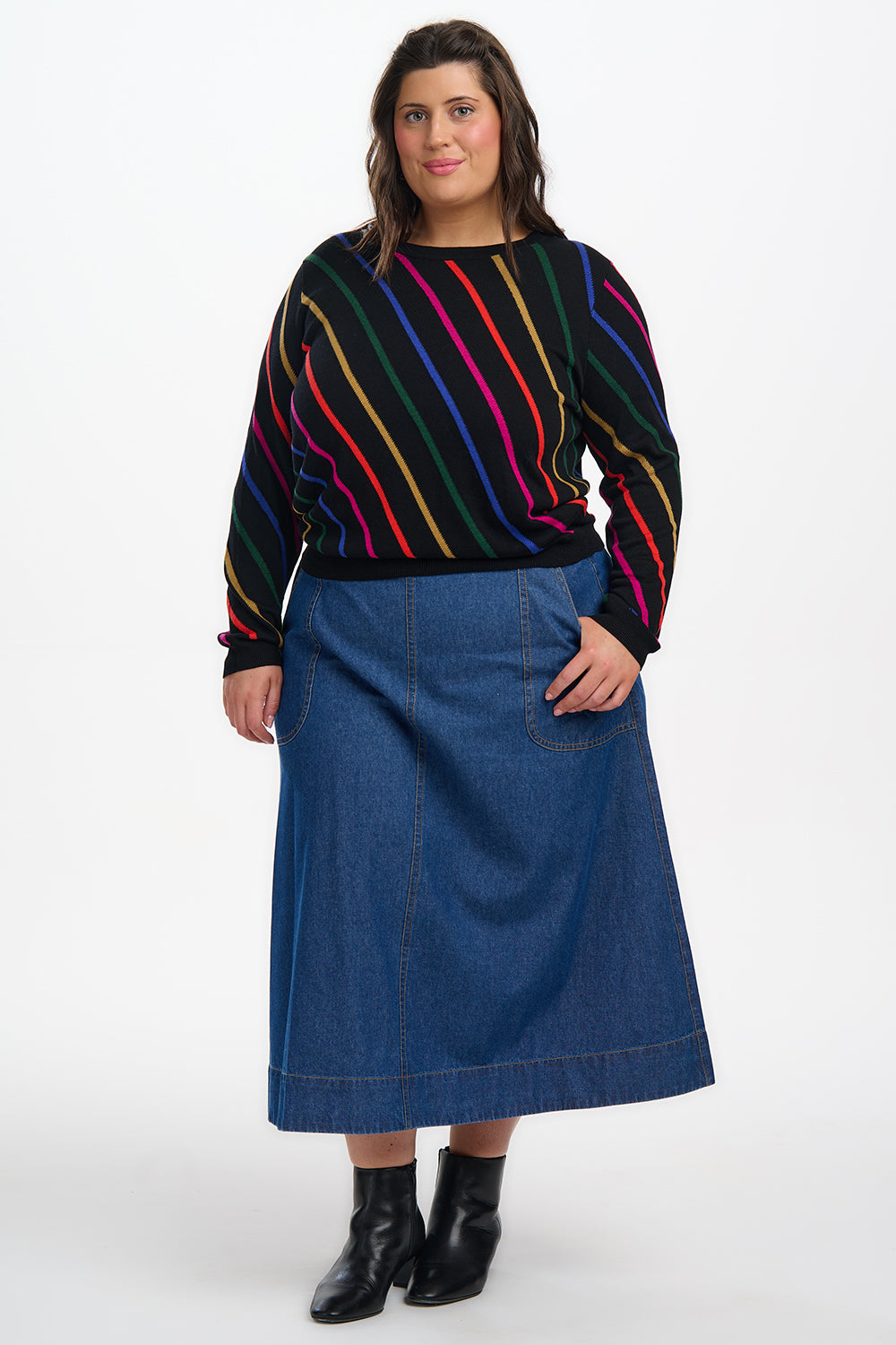 Woman wearing a colorful striped sweater and blue denim skirt on a white background
