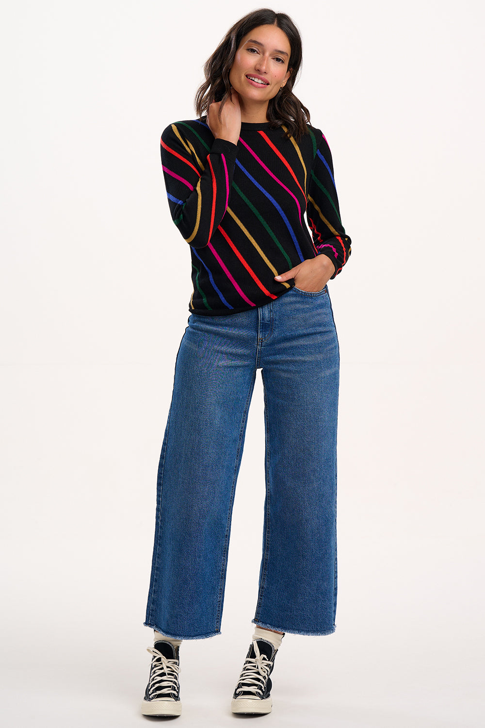 Woman wearing a colorful striped sweater and blue jeans on a white background