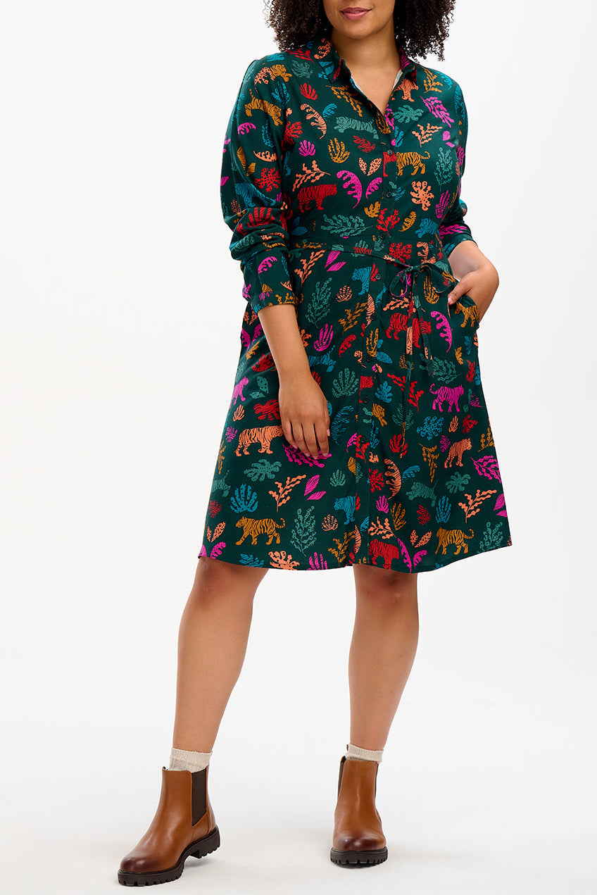 A woman standing and posing in a dark green shirt dress with a tie waist belt and a short skirt, featuring a tiger cutouts print.