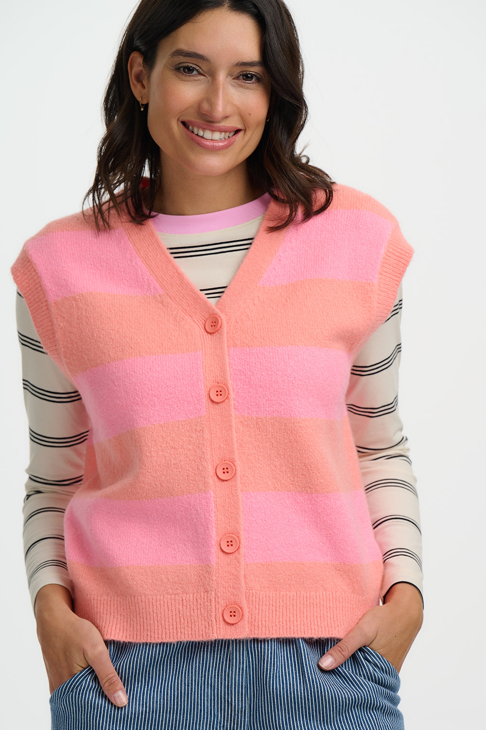 Woman wearing a pink and peach striped cardigan over a striped shirt on a white background