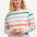 A woman wearing an off-white long-sleeve t-shirt with a thin rainbow stripe pattern over an off-white base, paired with jeans.