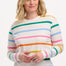 A woman wearing an off-white long-sleeve t-shirt with a thin rainbow stripe pattern over an off-white base, paired with jeans.