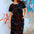 Woman wearing a black floral dress in front of a graffiti-covered wall.