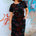 Woman wearing a black floral dress in front of a graffiti-covered wall.