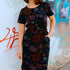 Woman wearing a black floral dress in front of a graffiti-covered wall.