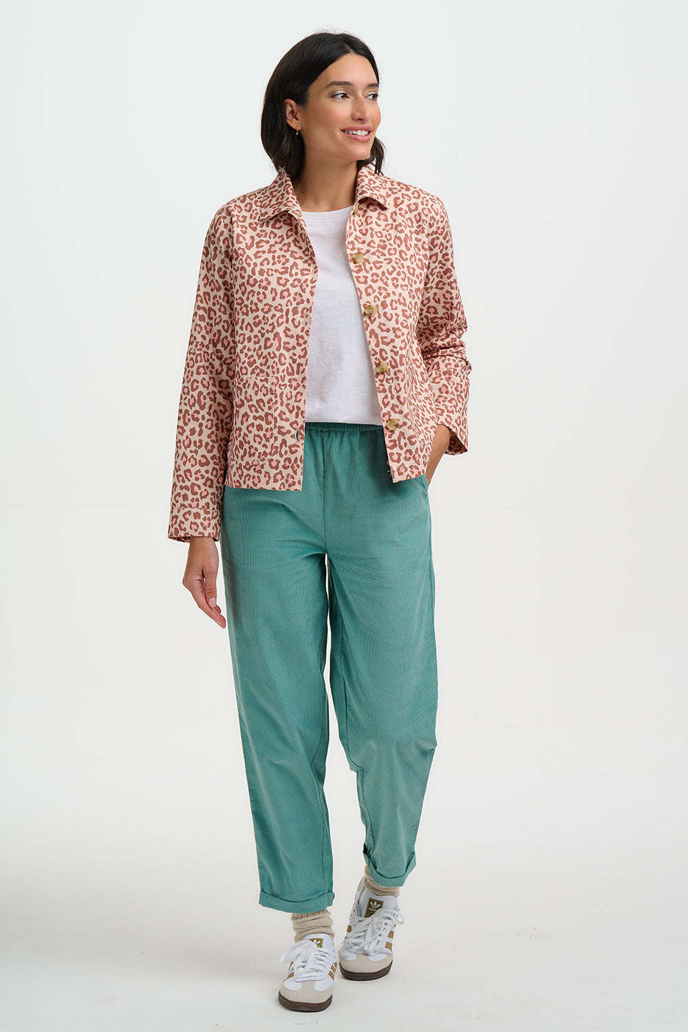 Woman wearing a patterned jacket, white shirt, green pants, and white sneakers on a white background