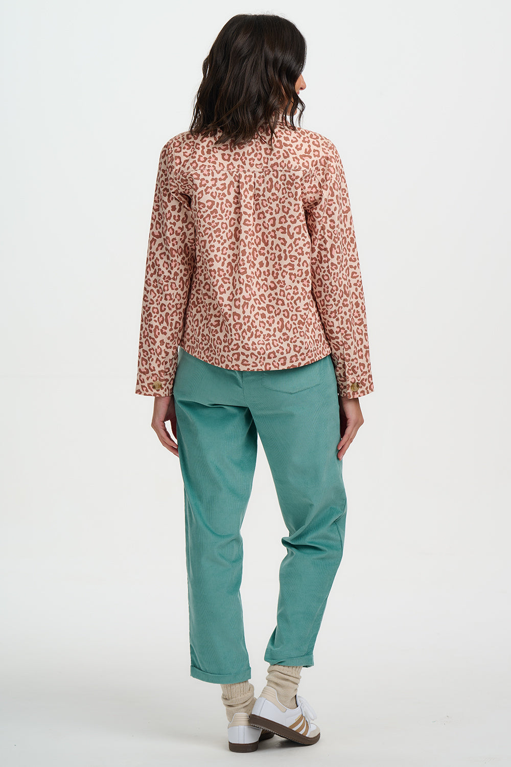 Person wearing a patterned top and teal pants on a white background