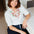 Woman wearing a white blouse with red floral embroidery sitting on a couch.