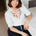 Woman wearing a white blouse with red floral embroidery sitting on a couch.