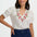 Woman wearing a white blouse with floral embroidery and navy pants on a white background
