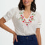 Woman wearing a white blouse with floral embroidery and navy pants on a white background