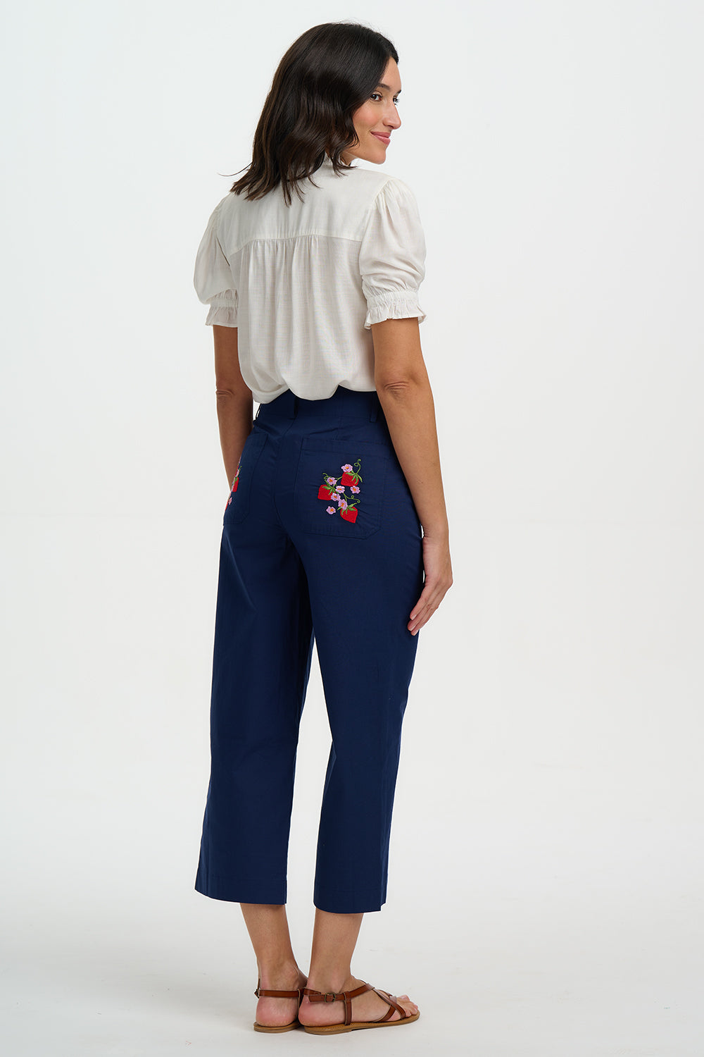 Woman wearing navy pants with a floral embroidery detail on a white background