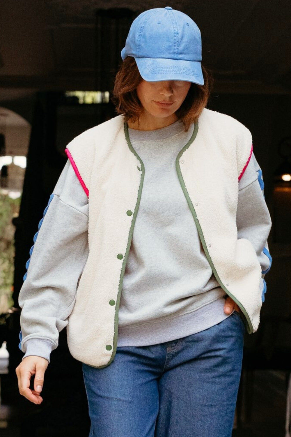 Person wearing a light gray fleece jacket with pink accents, blue jeans, and a blue cap.