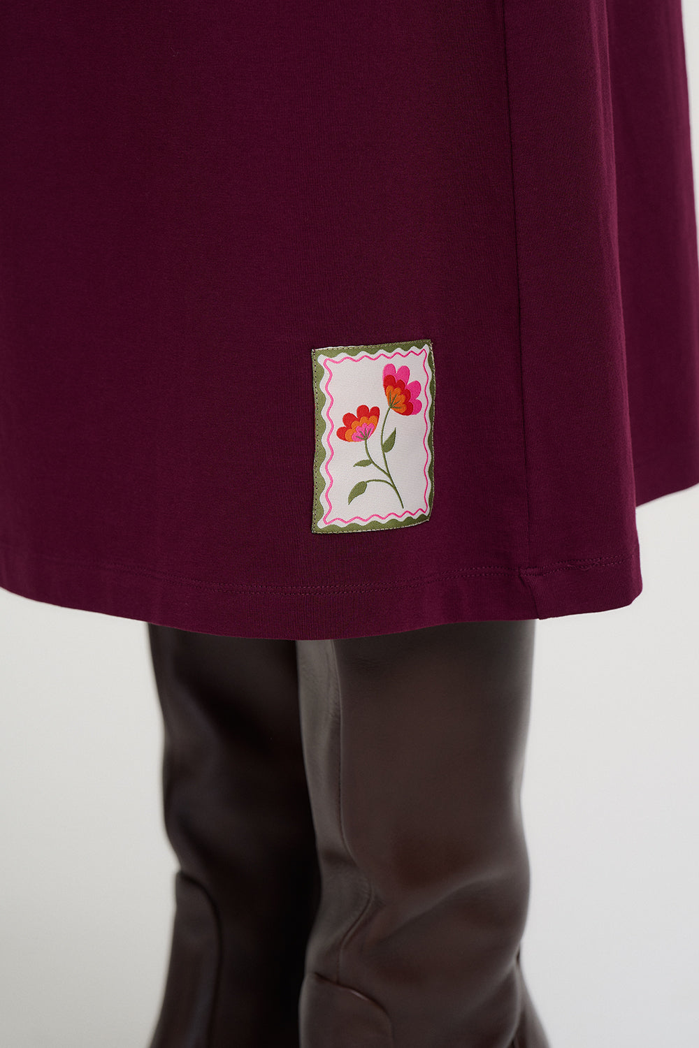 Close-up of a maroon garment with a floral patch on a white background