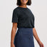 A woman modeling a dark charcoal gray short-sleeve knit top and a dark blue denim mini skirt with a scalloped hem and front patch pocket, against a light gray studio background.