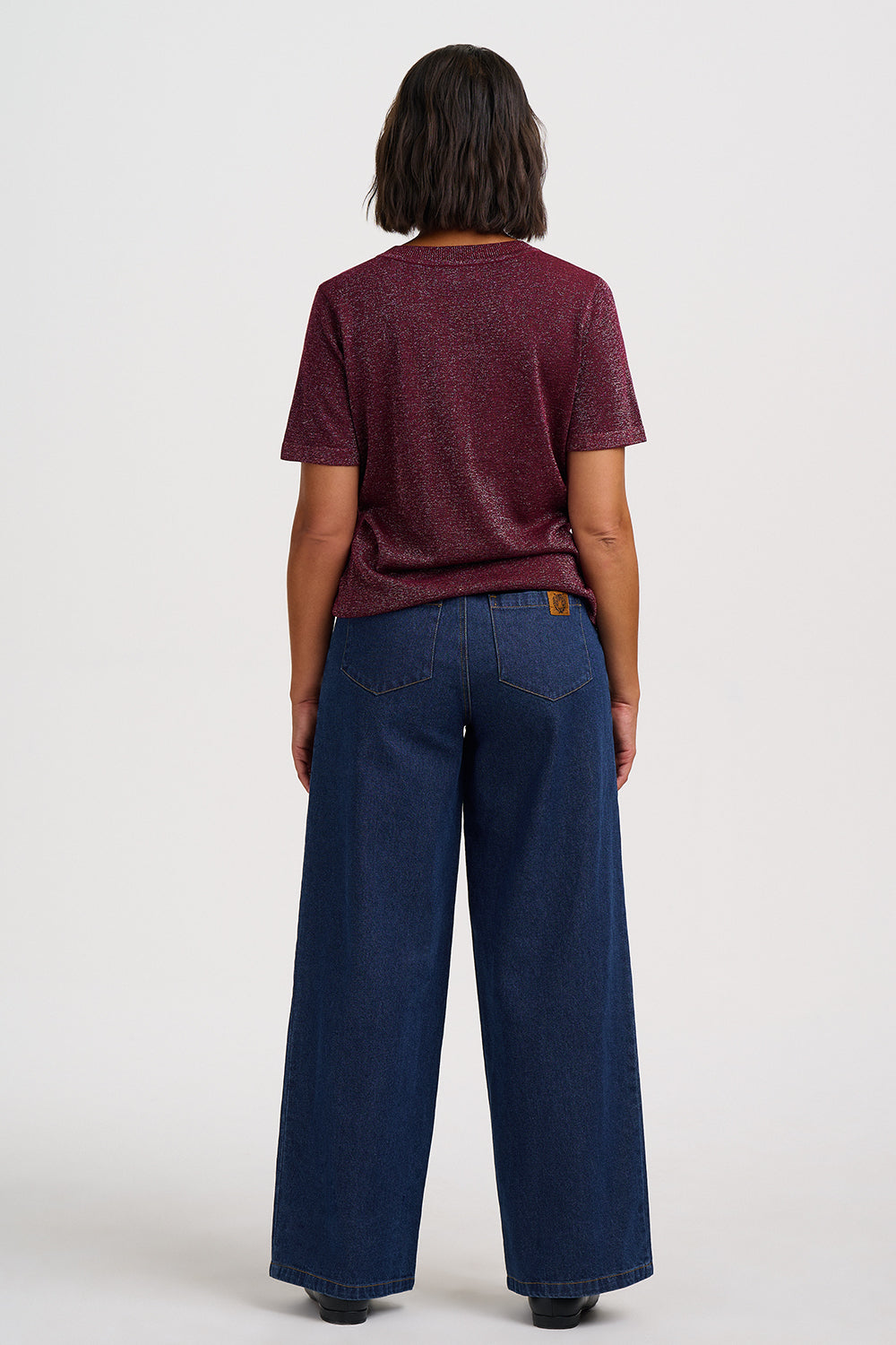 A model shown from the back wearing a maroon short-sleeve t-shirt and dark blue wide-leg jeans against a plain light gray background.