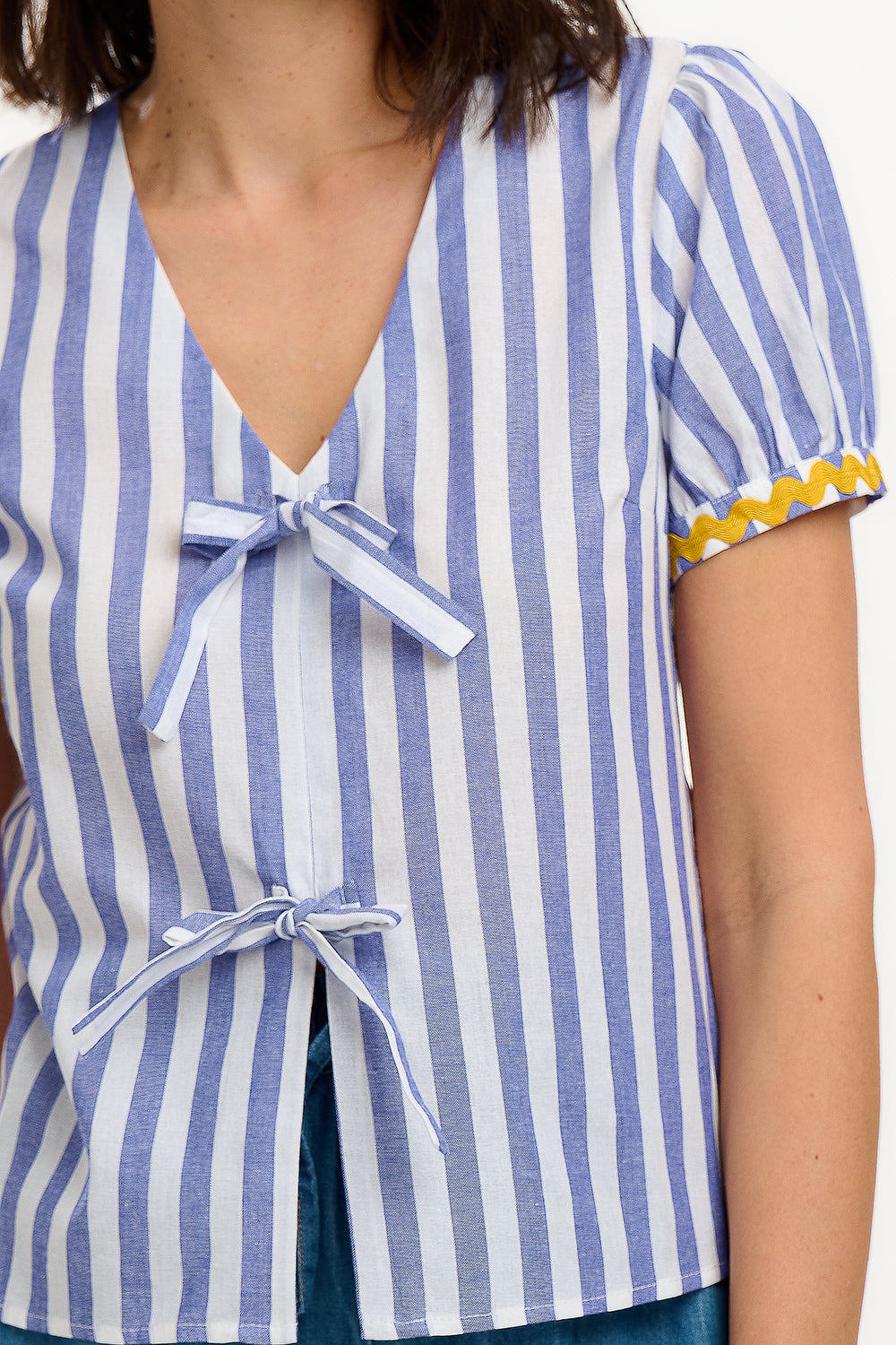 A woman smiling and wearing an off-white and blue striped top with short puff sleeves and a decorative bow tie at the v-neck.
