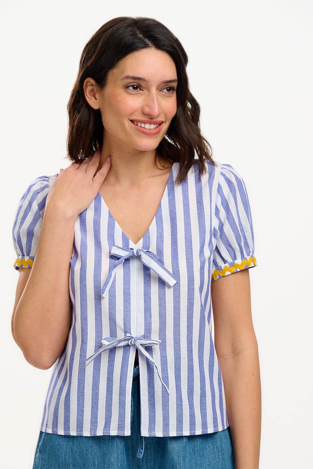 A woman smiling and wearing an off-white and blue striped top with short puff sleeves and a decorative bow tie at the v-neck.