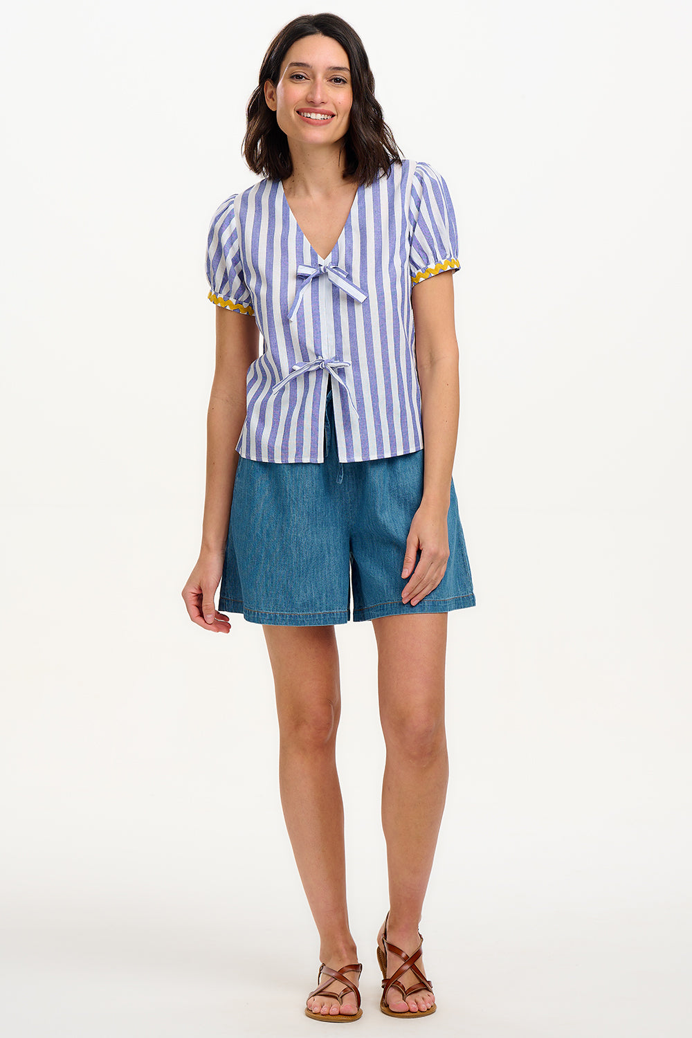A woman smiling and wearing an off-white and blue striped top with short puff sleeves and a decorative bow tie at the v-neck.