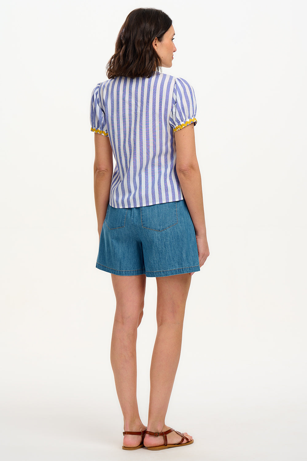 A woman smiling and wearing an off-white and blue striped top with short puff sleeves and a decorative bow tie at the v-neck.