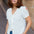 Woman wearing a white blouse with floral embroidery and blue jeans on a street.