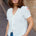 Woman wearing a white blouse with floral embroidery and blue jeans on a street.