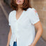 Woman wearing a white blouse with floral embroidery and blue jeans on a street.