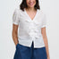 Woman wearing a white blouse with ruffles and blue shorts on a white background