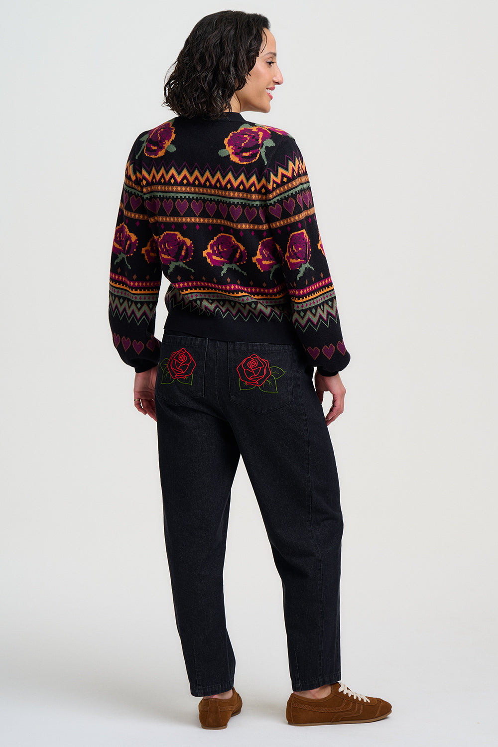Person wearing a patterned sweater and dark pants on a white background