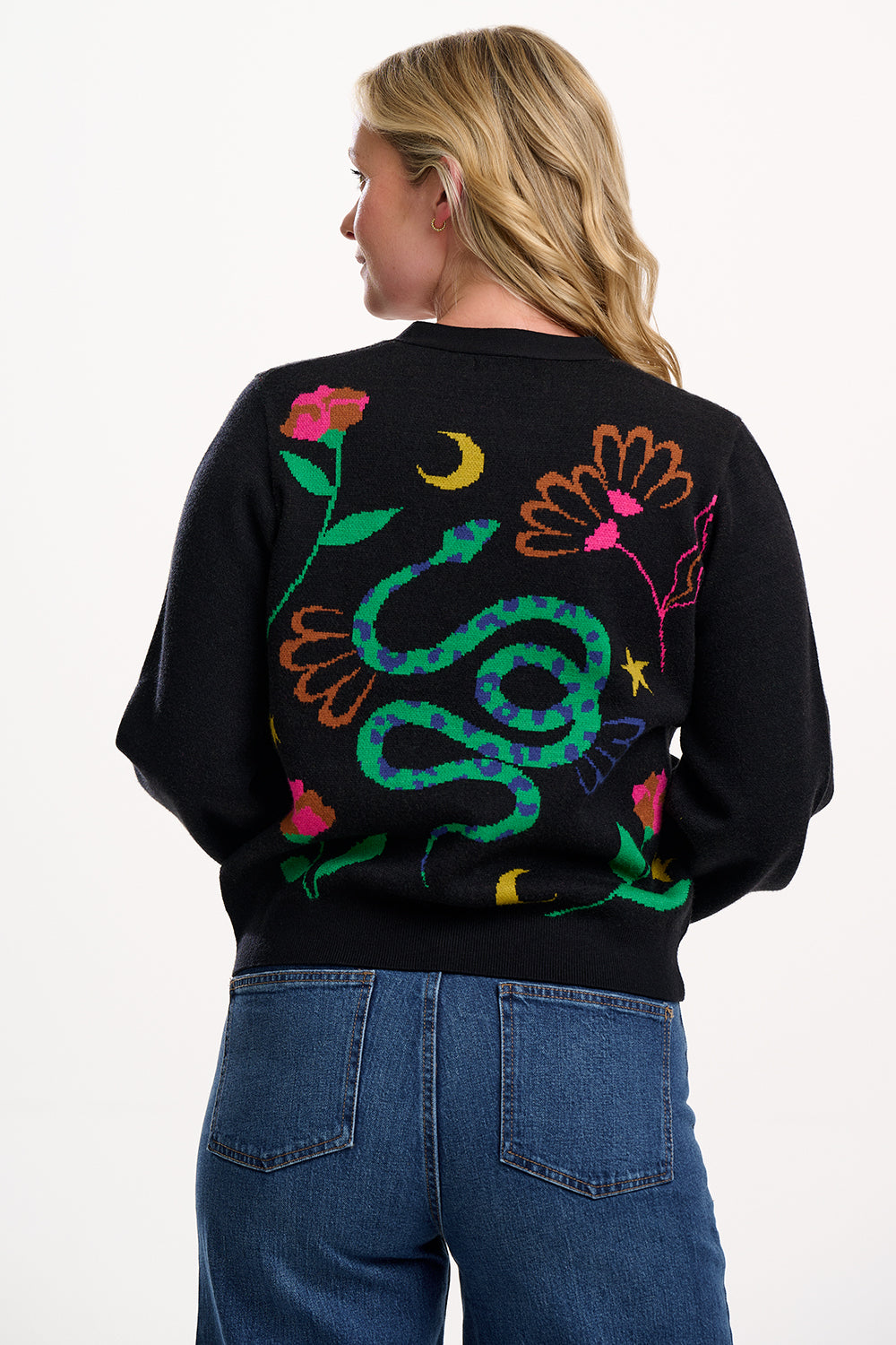 Person wearing a black sweater with colorful snake and floral designs on the back, standing against a white background.
