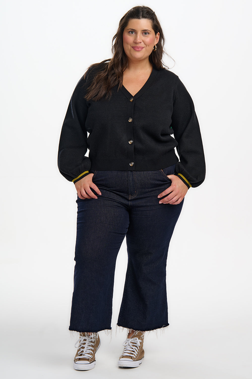 Woman wearing a black cardigan and dark jeans on a white background