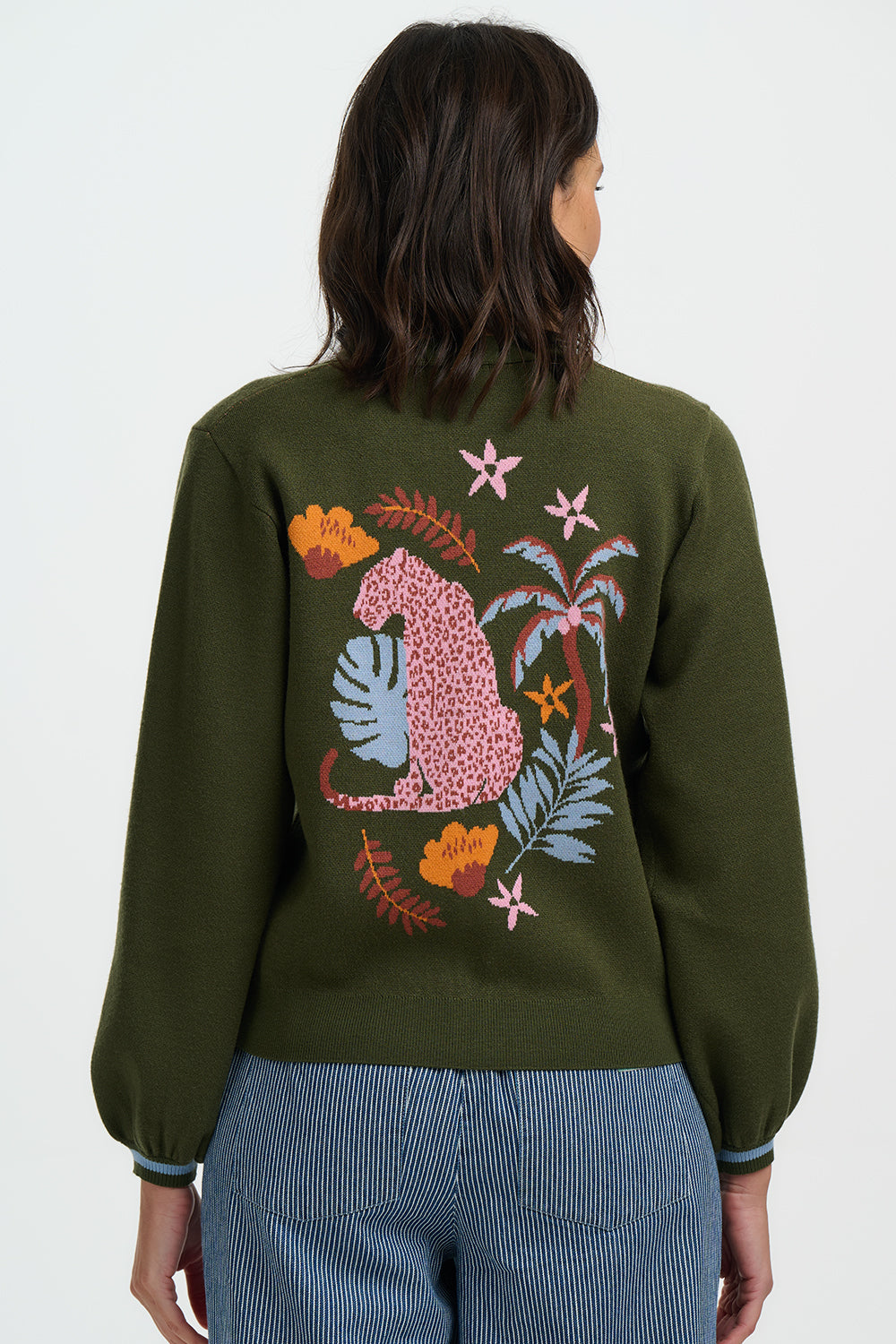 Person wearing a green sweater with a colorful animal and floral design on the back against a white background