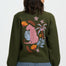 Person wearing a green sweater with a colorful animal and floral design on the back against a white background