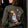 Person wearing a green sweatshirt with colorful designs on the back, standing indoors.