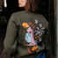 Person wearing a green sweatshirt with colorful designs on the back, standing indoors.