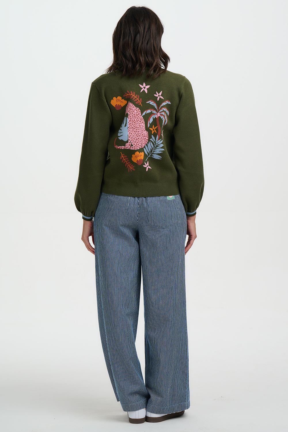 Person wearing a green sweater with a colorful design on the back, standing against a white background