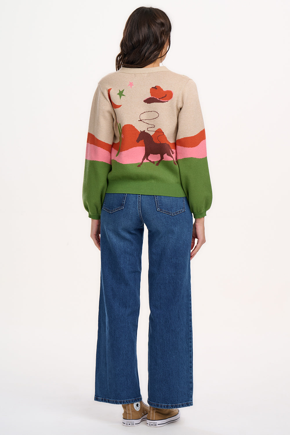 Sugarhill Brighton model wearing a beige cardigan with a cowgirl-themed graphic design, including images of cacti, cowboy hats, and horses.