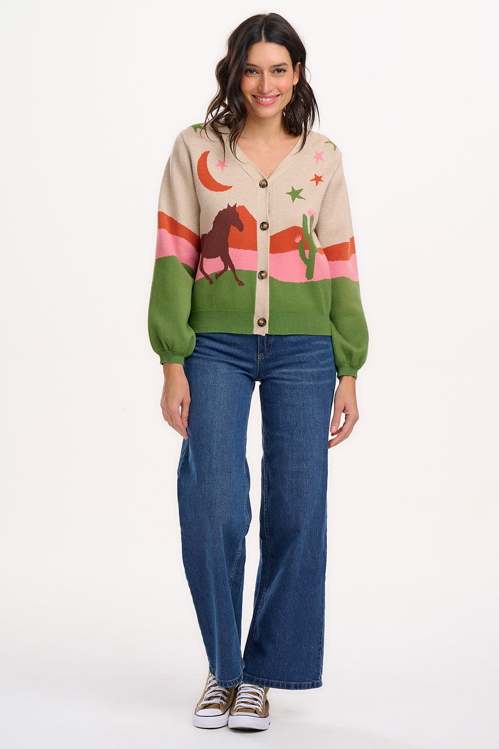 Sugarhill Brighton model wearing a beige cardigan with a cowgirl-themed graphic design, including images of cacti, cowboy hats, and horses.