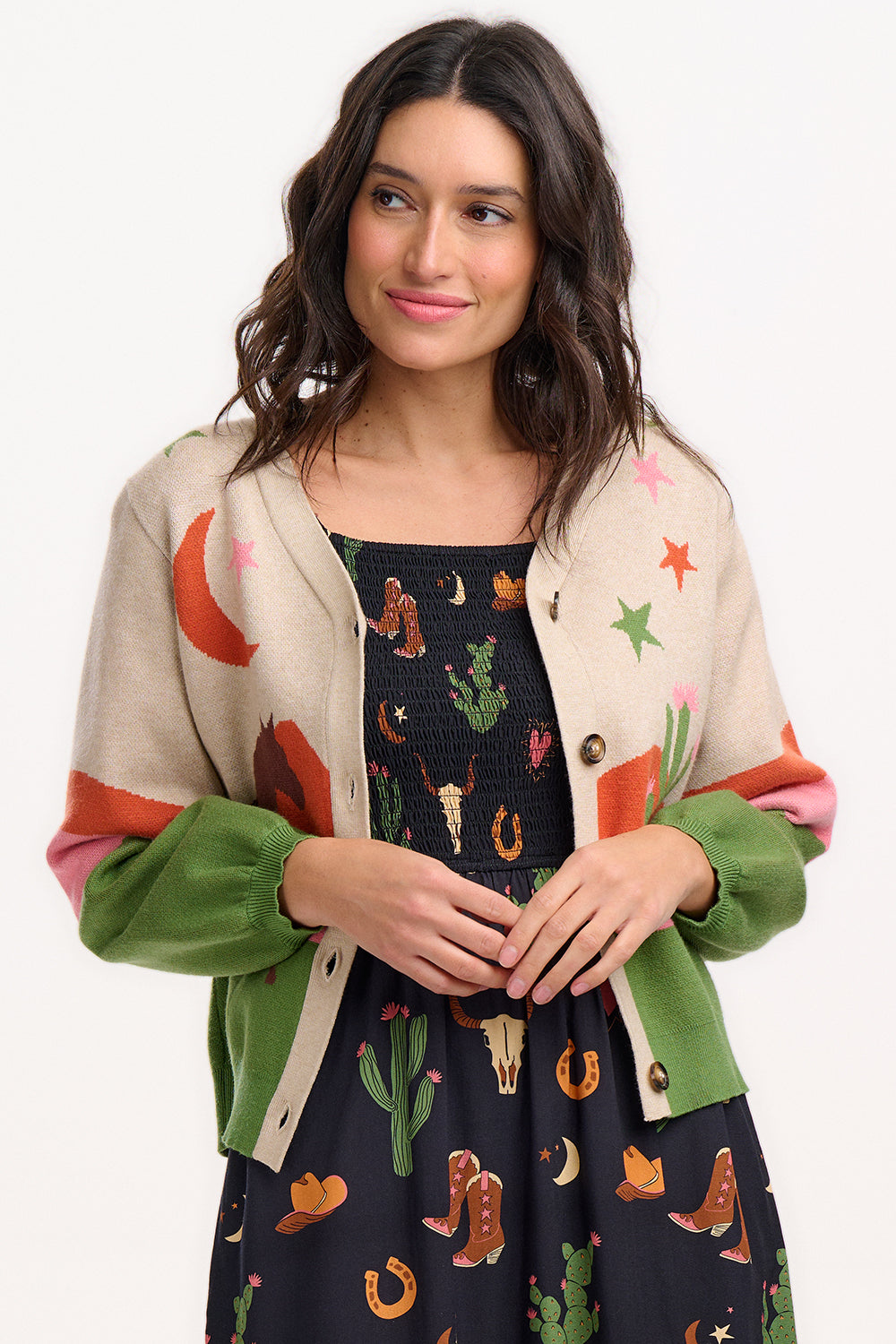 Sugarhill Brighton model wearing a beige cardigan with a cowgirl-themed graphic design, including images of cacti, cowboy hats, and horses.