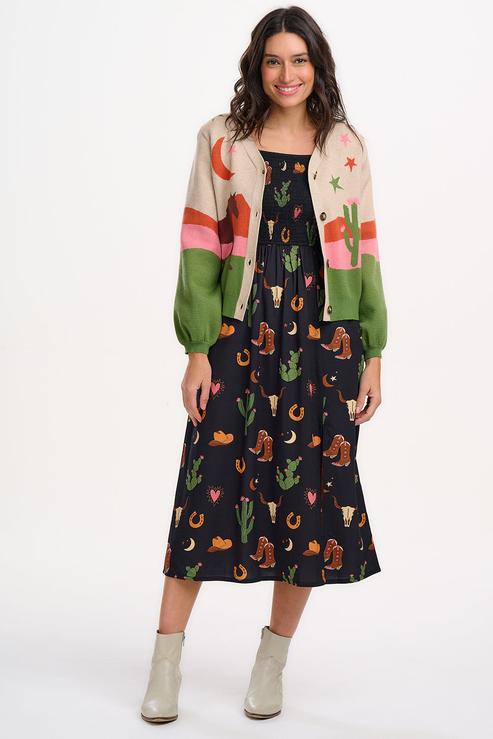 Sugarhill Brighton model wearing a beige cardigan with a cowgirl-themed graphic design, including images of cacti, cowboy hats, and horses.