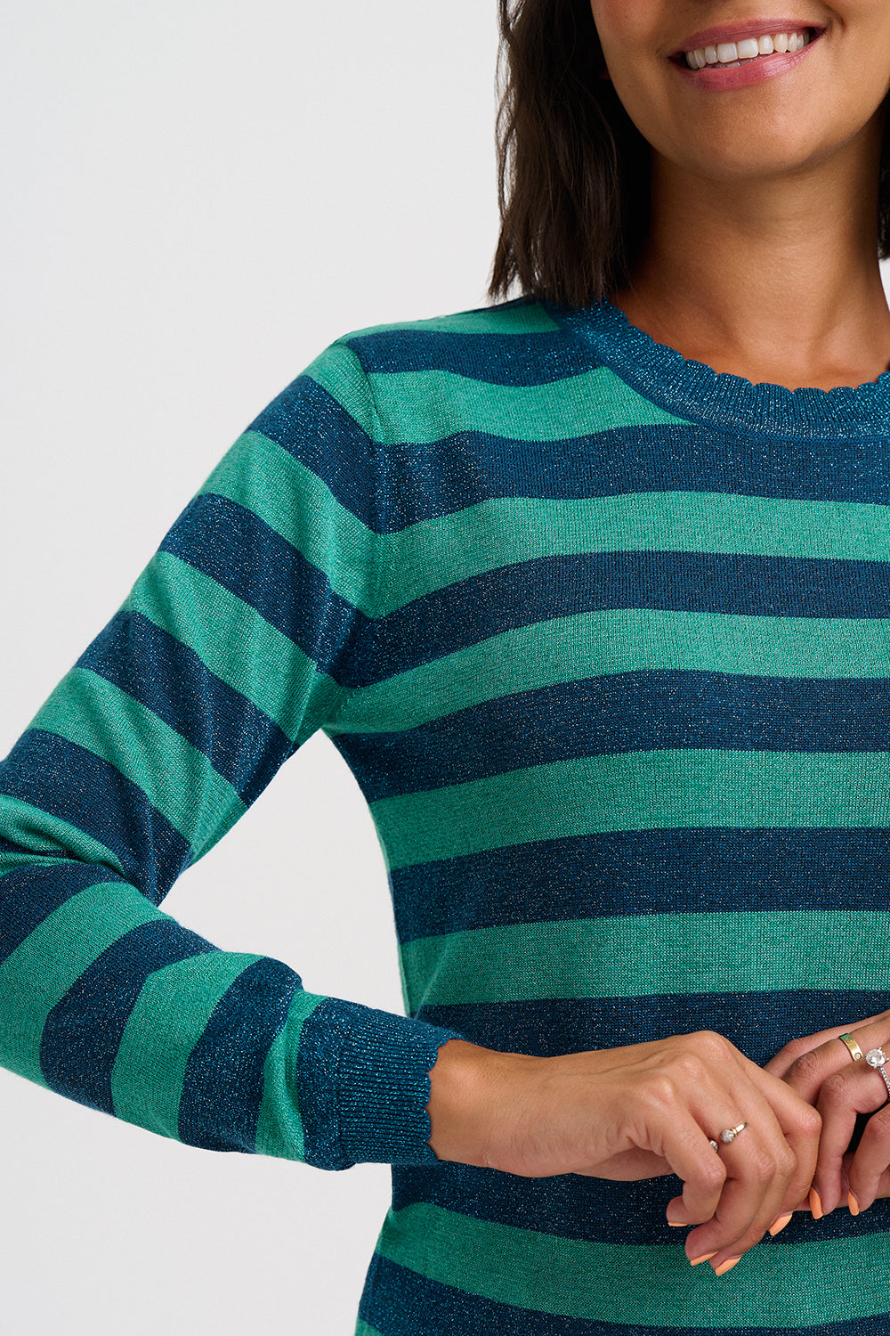 A close-up of a woman wearing a long-sleeve knit top with horizontal stripes in teal green and dark navy blue, against a light gray background.