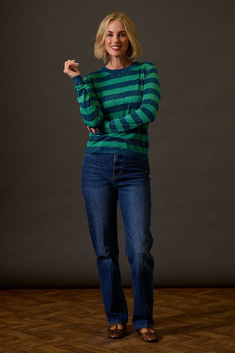 Woman wearing a green and blue striped sweater and blue jeans against a dark background