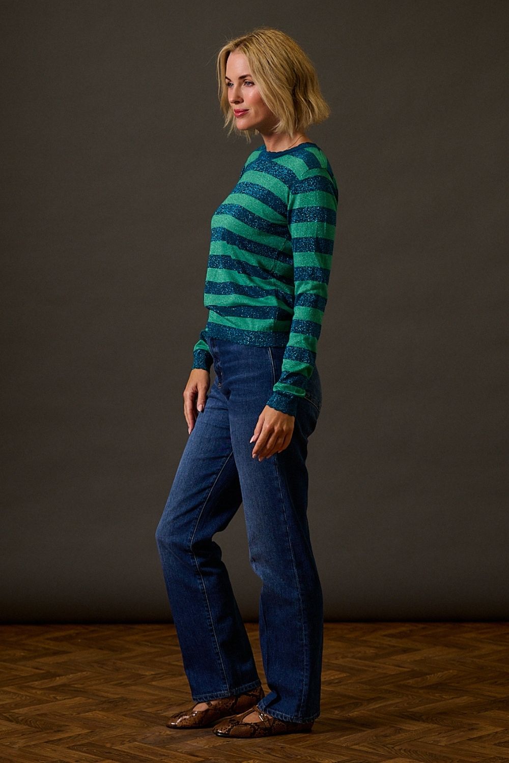 Woman wearing a blue and green striped sweater and blue jeans against a dark background