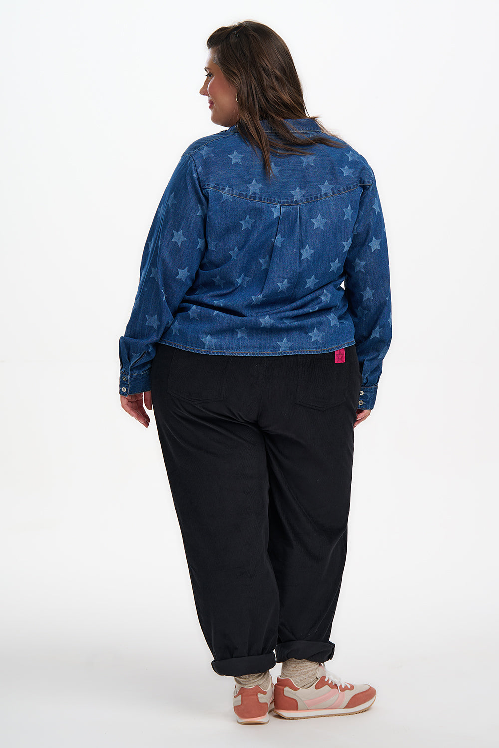Person wearing a blue denim jacket with star pattern and black pants on a white background