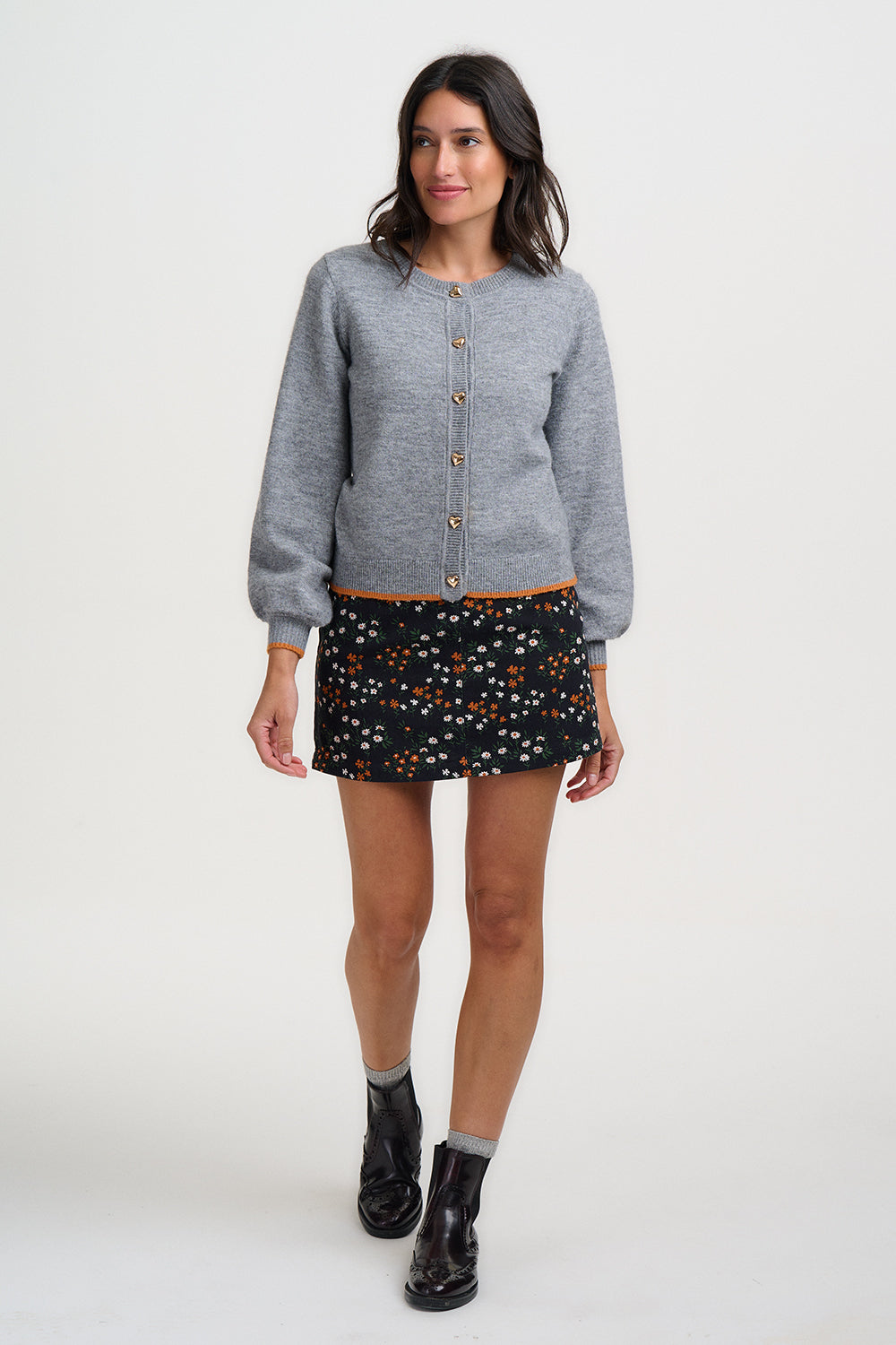 Woman wearing a gray cardigan, patterned skirt, and black boots on a white background