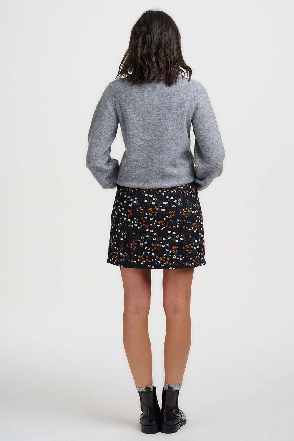 Person wearing a gray sweater and patterned skirt on a white background